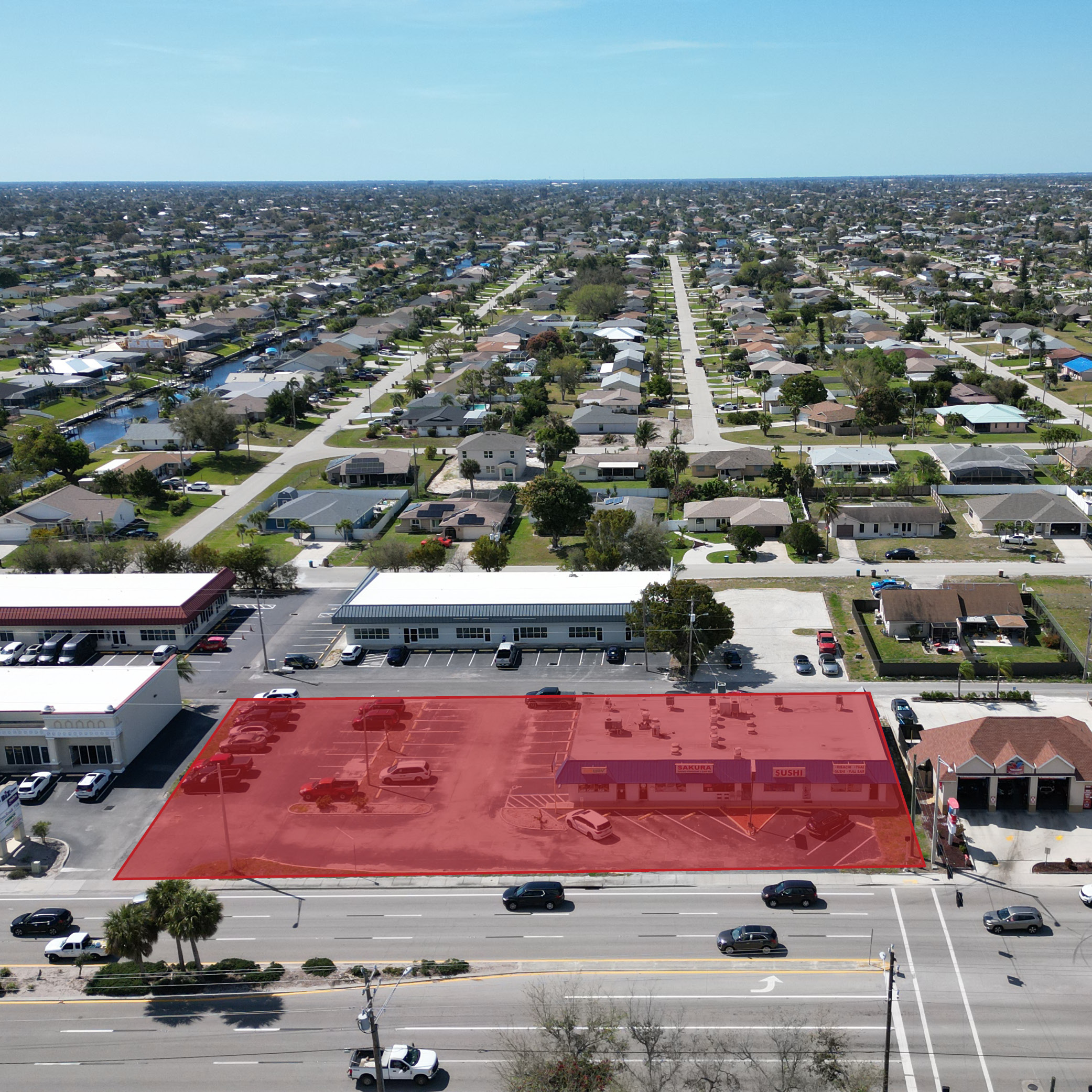 Aerial view of a commercial property highlighted in red along a main road, surrounded by other buildings and a residential neighborhood.