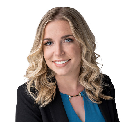 A woman with wavy blonde hair, wearing a blue top and black blazer, smiling at the camera against a white background.