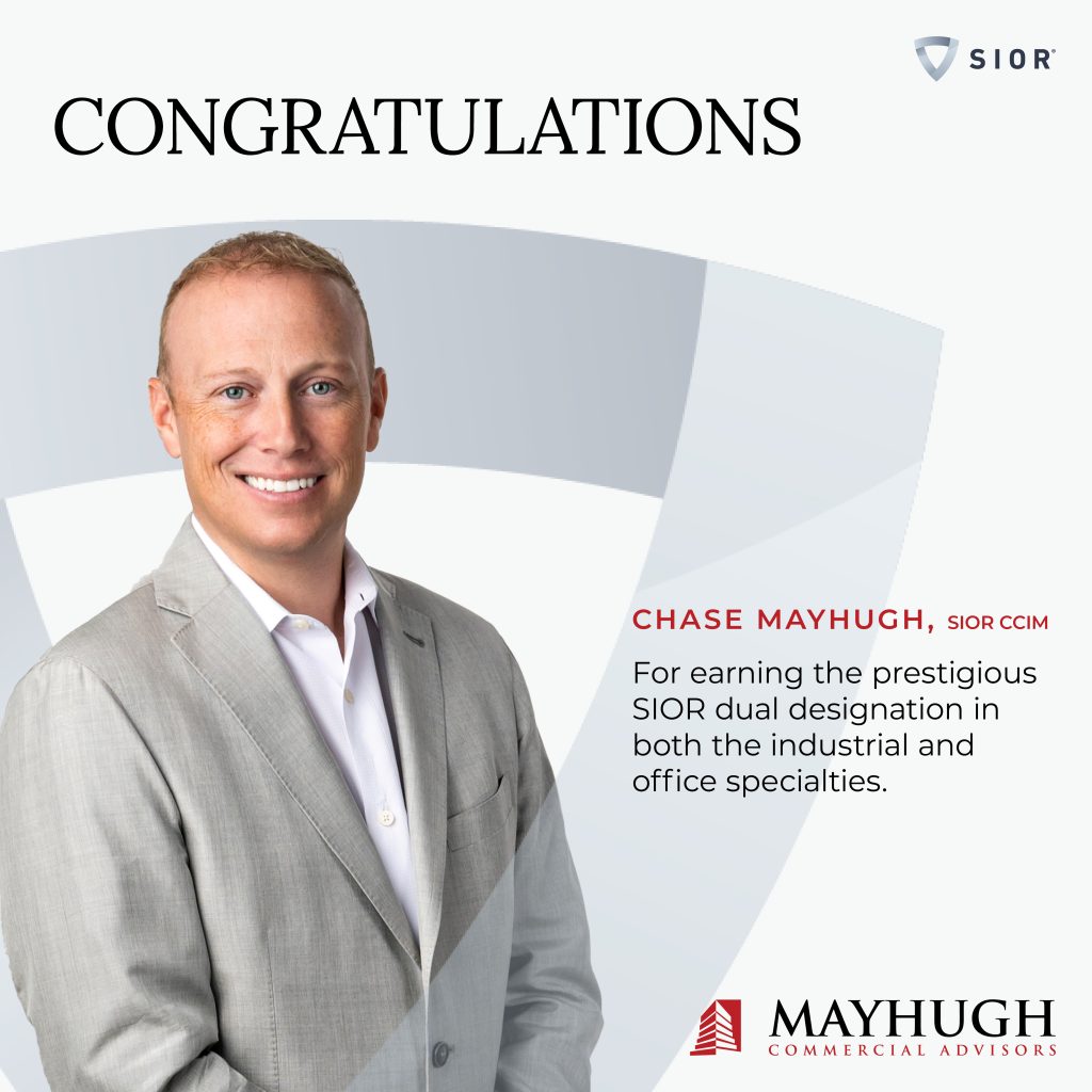 A man in a light gray suit smiles at the camera next to text congratulating Chase Mayhugh for earning the SIOR dual designation in industrial and office specialties. Mayhugh Commercial Advisors logo appears.