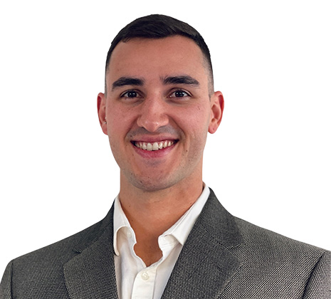 A man wearing a gray suit jacket and white shirt smiles at the camera against a plain white background.