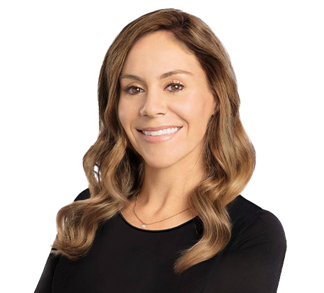 Smiling woman with long, wavy brown hair wearing a black top, photographed against a white background.