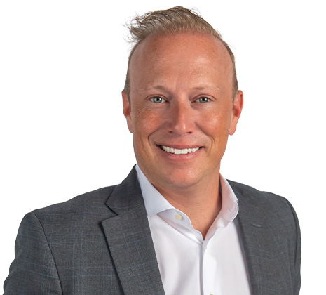 Smiling man with light skin and blond hair wearing a gray suit jacket and white dress shirt, posing in front of a white background.