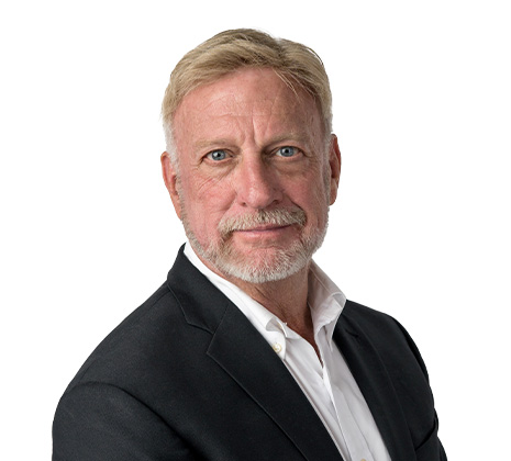 A middle-aged man with light hair and beard wearing a white shirt and dark blazer, posing against a plain white background.