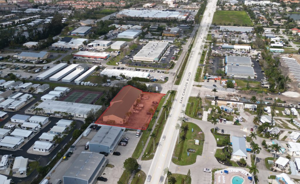 Aerial view of a commercial area with a large building and surrounding lot highlighted in red along San Carlos Blvd, bordered by other buildings and roads.