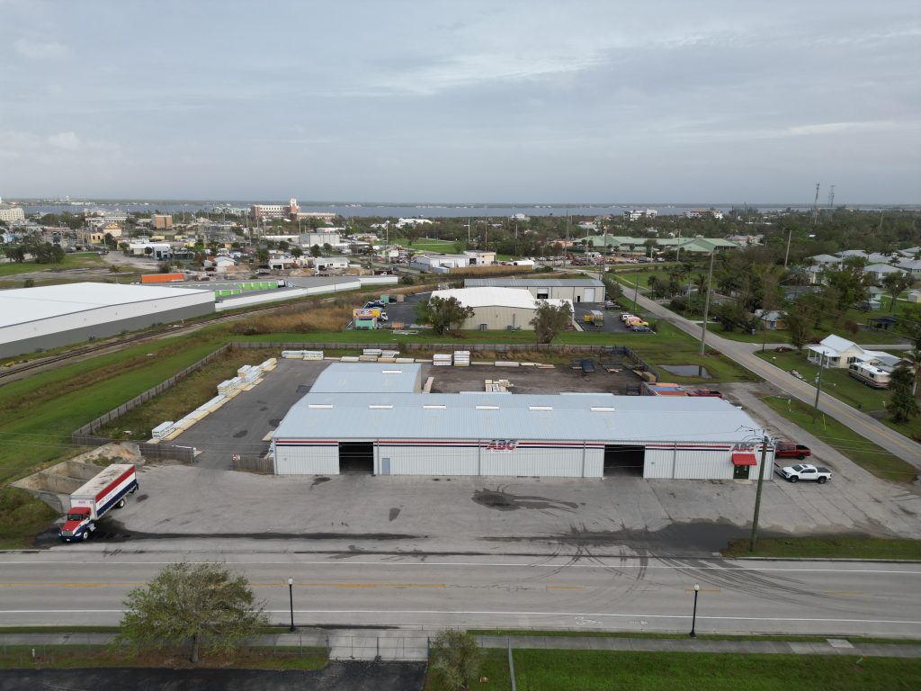 Aerial view of a large warehouse building with a truck in the parking lot, surrounded by roads and other commercial structures.
