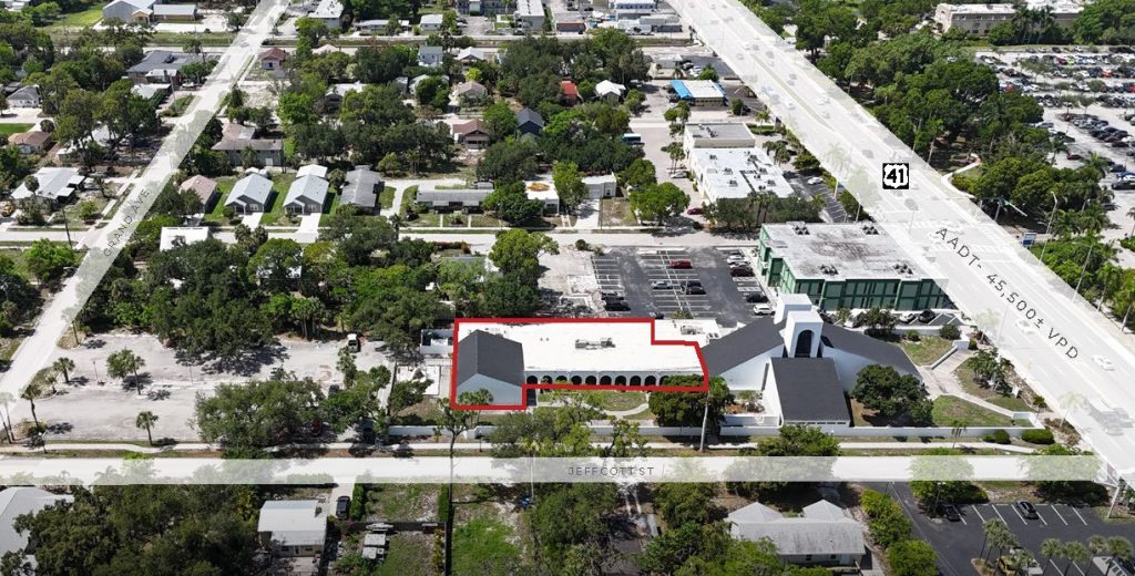 Aerial view of a commercial area with a white building outlined in red, parking lots, roads, and surrounding trees. Major road labeled US 41 is visible on the right.